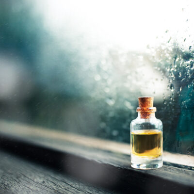 梅雨の季節の雨に濡れた窓辺に置かれたアロマオイルのボトル