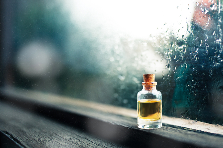 梅雨の季節の雨に濡れた窓辺に置かれたアロマオイルのボトル